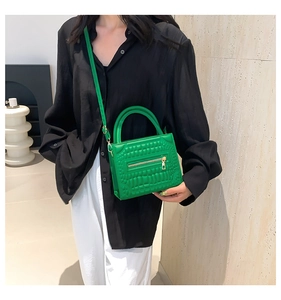 Detailed close-up of green crocodile pattern handbag with gold zipper and dual handles