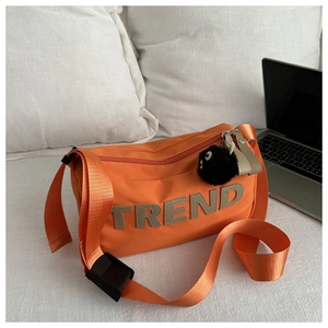 Close-up of orange canvas bag with TREND lettering and black plush charm on white bedding