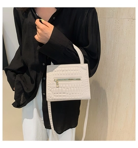 Detail of cream faux leather handbag featuring a textured crocodile pattern and metal zipper