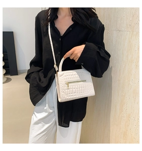 Detail of white crocodile pattern handbag with gold hardware and top handle shown on model
