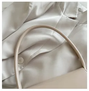 Gros plan d'un sac à main beige en cuir brillant avec poignée cylindrique et coutures fines