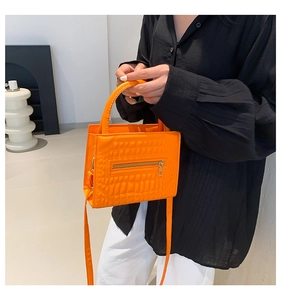 Detail of bright orange crocodile embossed handbag featuring gold zipper and metal hardware