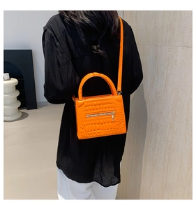 Detail of bright orange crocodile embossed handbag with metal zipper and leather strap