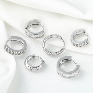 Trois paires de boucles d'oreilles créoles argentées avec zircons sur soie blanche