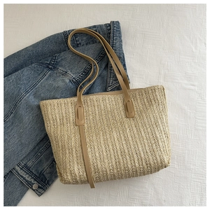 Detail of straw woven tote bag with brown PU leather straps on denim background