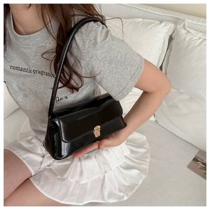 Close-up of a glossy black patent leather shoulder bag with a gold metallic buckle