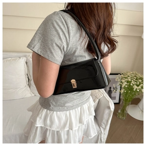 Detail view of a black glossy underarm bag with a golden buckle on a shoulder strap