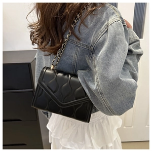 Dettaglio di una borsa a tracolla nera trapuntata a onde con catena dorata su modella