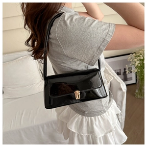 Glossy black underarm bag with gold hardware shown on a model in a minimalist setting