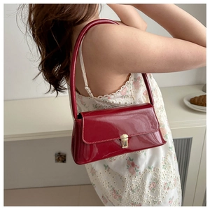 Detail view of burgundy patent leather baguette bag with gold buckle on lace dress