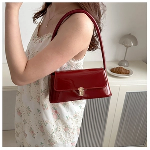 Détail d'un sac baguette en cuir verni rouge foncé avec une boucle en métal doré pour femme