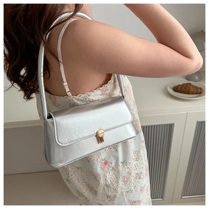 Close-up of metallic silver baguette bag with a golden rectangular clasp on a model