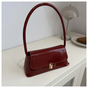 Detail of dark red patent leather baguette bag with gold metal clasp and sleek handle