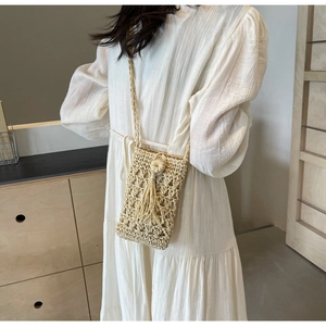 Détail d'un sac à téléphone en paille tissée avec pompon décoratif sur robe blanche texturée
