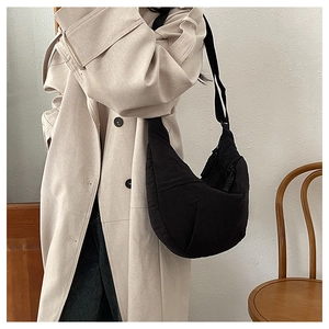Detail of black nylon crescent bag worn with a beige trench coat for a minimalist style