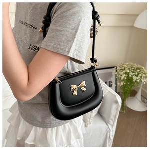 Minimalist black saddle bag with golden bow and knotted strap on female model
