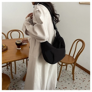 Detail of a black nylon dumpling bag with adjustable wide strap shown on a model