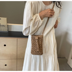 Détail de la pochette de téléphone en paille tressée avec pompons et bandoulière