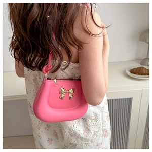 Detail of bright pink crossbody bag with golden bow and thin shoulder strap worn by model