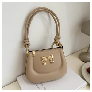 Close-up of beige leather shoulder bag featuring a golden metal bow and knot detail