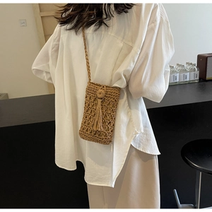 Sac de téléphone en paille tissée avec détail de gland et motif ajouré sur un mannequin