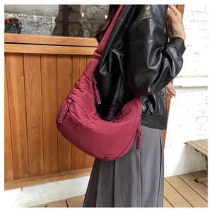 Detail of burgundy nylon dumpling bag showing braided zipper pulls and wide strap