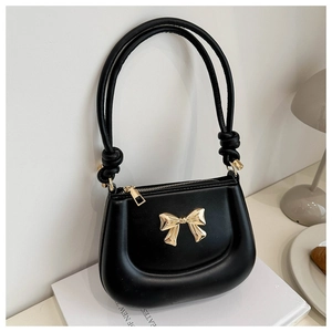 Detail of black saddle bag featuring a golden metal bow and stylish knotted shoulder strap