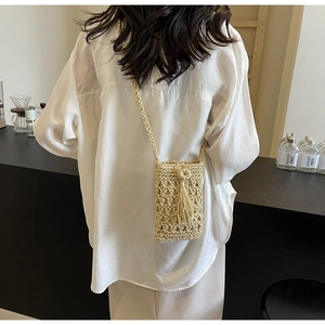 Sac bandoulière en paille évidée pour téléphone avec pompon porté par un mannequin