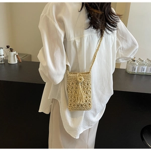 Gros plan sur le sac de téléphone en paille beige avec franges sur chemise blanche