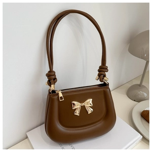 Brown leather underarm bag with gold bow ornament and puffed bottom on white background