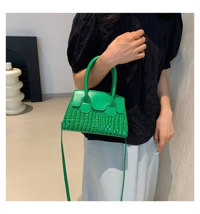 Detail of a bright green mini trapezoid handbag with crocodile pattern held by a person