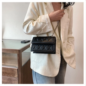 Détail du sac à chaîne noir embossé porté par un mannequin en blazer blanc élégant