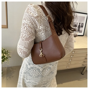 Close-up of brown leather crescent shoulder bag with golden metallic hook clasp detail