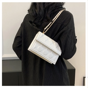 Détail d'un sac à bandoulière blanc matelassé avec texture larme et chaîne dorée