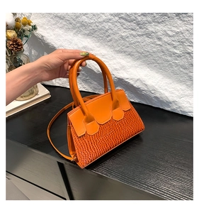 Detail of orange faux-crocodile handbag with textured paneling and dual top handles