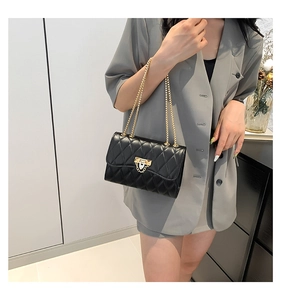 Detail of black quilted chain bag with gold V-shape buckle and leather texture