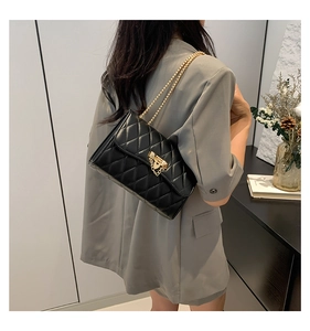 Detail of a black quilted crossbody bag with gold chain strap worn by a model