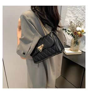 Detail of a black quilted crossbody bag with gold chain and metal lock on a model