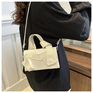 Détail macro du sac bandoulière en toile crème avec nœud décoratif et textures de tissu