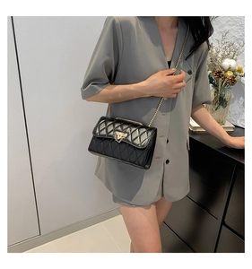 Quilted black chain crossbody bag with gold heart lock shown on a gray suit model