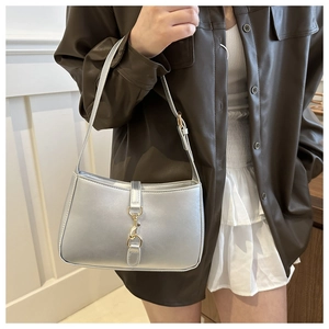 Detail of silver underarm bag featuring glossy finish and elegant golden clasp closure