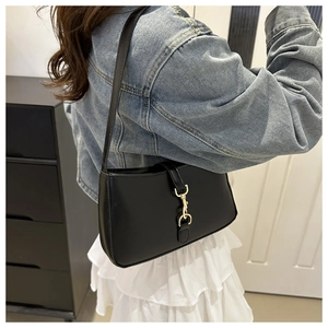 Detail of minimalist black leather underarm bag with iconic vintage gold spring buckle lock