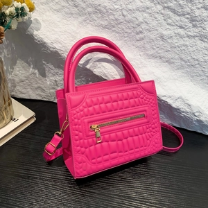 Pink crocodile pattern handbag with gold hardware and adjustable strap on rock background