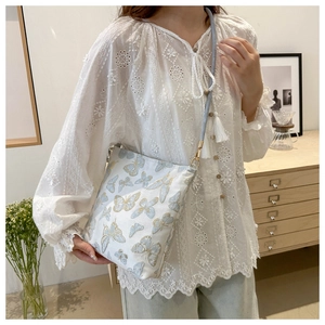 Detail of white canvas crossbody bag featuring exquisite blue and gold butterfly embroidery
