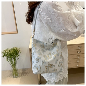 Detailed close-up of a white tote bag featuring blue butterfly embroidery on a model