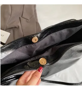 Detail of glossy black patent leather tote bag with gold magnetic buckle and fabric lining