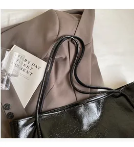Detail of black glossy patent leather tote bag with crinkle texture on a brown blazer