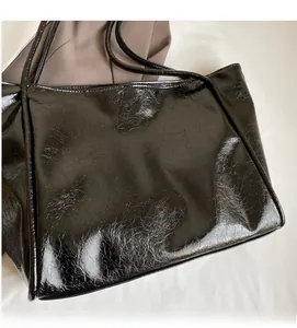Close-up of black glossy tote bag featuring a pleated texture and slim shoulder straps