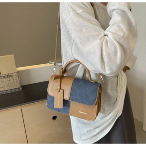 Detail of a color-block crossbody bag featuring brown faux leather and blue denim patchwork