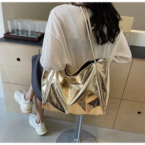 Chic metallic gold tote bag with textured surface shown on shoulder in minimalist setting